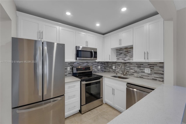 kitchen featuring light tile patterned floors, a sink, white cabinets, appliances with stainless steel finishes, and backsplash