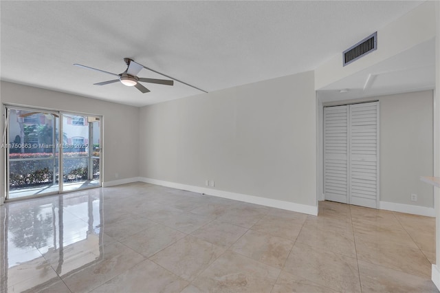 empty room featuring a textured ceiling, light tile patterned flooring, a ceiling fan, visible vents, and baseboards