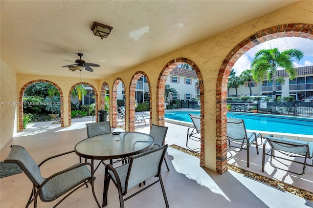 view of patio featuring a ceiling fan, fence, and a community pool