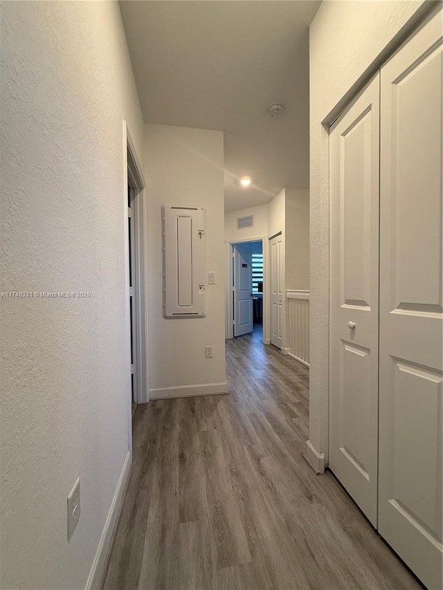 hallway with a textured wall, wood finished floors, visible vents, and baseboards