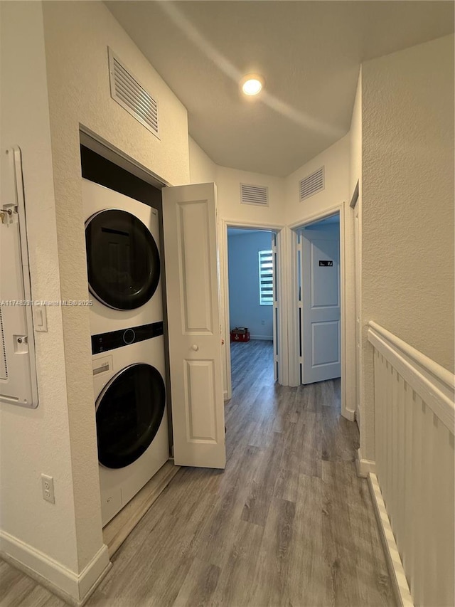 clothes washing area with visible vents, stacked washing maching and dryer, and wood finished floors