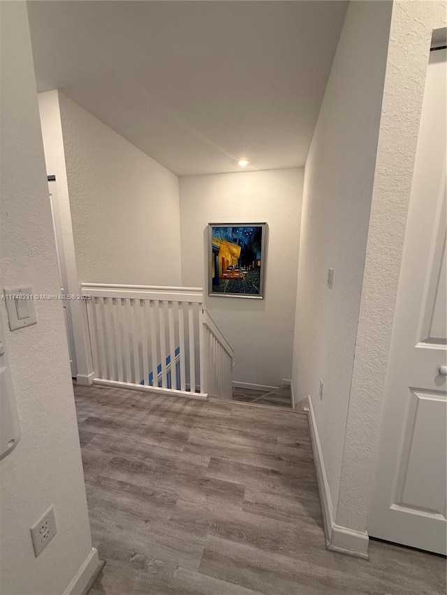 corridor featuring baseboards, a textured wall, an upstairs landing, and wood finished floors