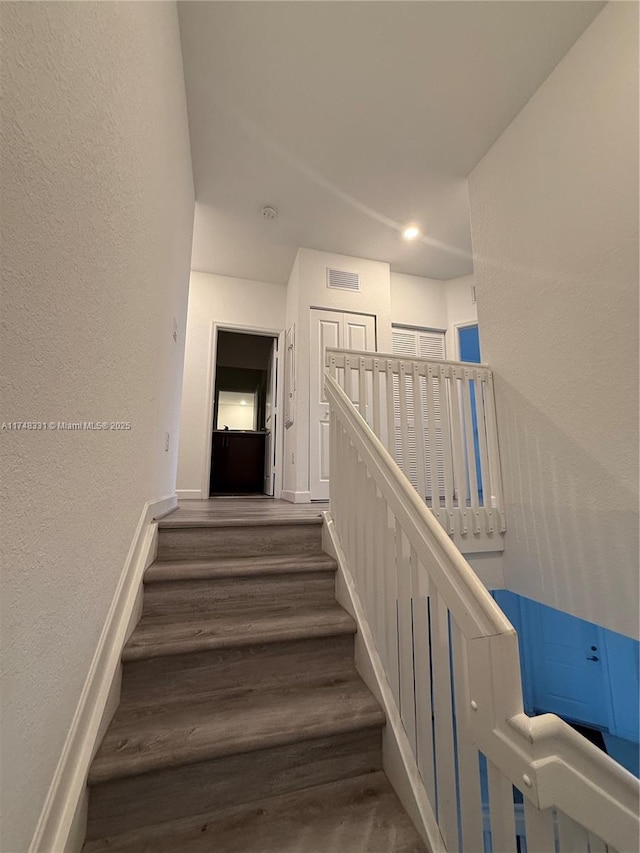 stairs with visible vents, a textured wall, baseboards, and wood finished floors