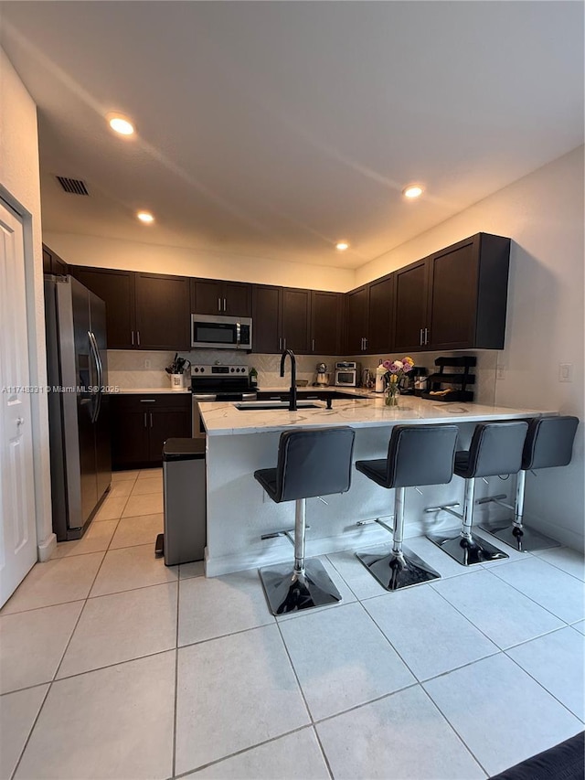 kitchen with light countertops, appliances with stainless steel finishes, a sink, a peninsula, and a kitchen bar