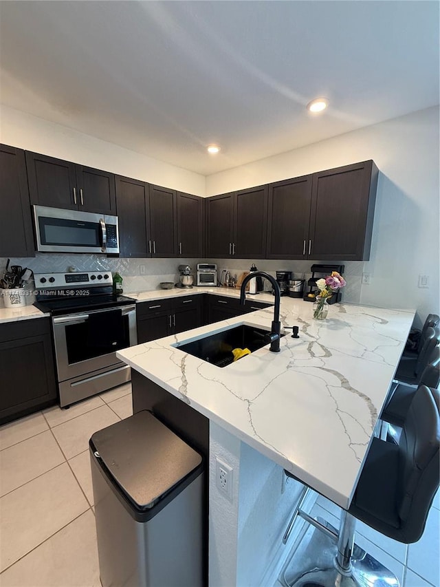 kitchen with a peninsula, a breakfast bar, a sink, appliances with stainless steel finishes, and light stone countertops