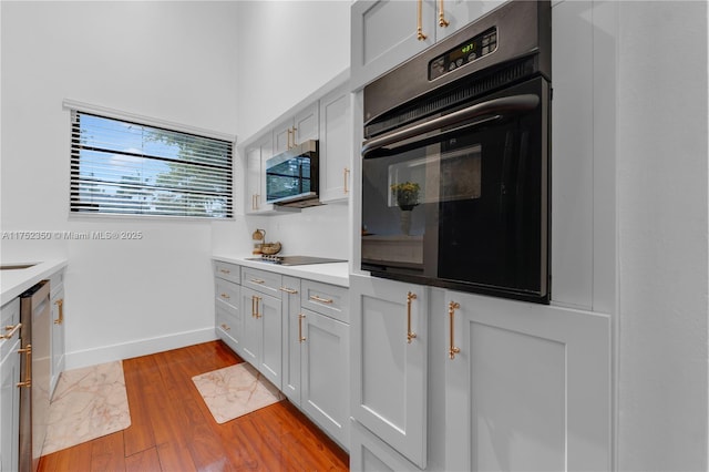 kitchen with baseboards, white cabinets, light wood-style flooring, light countertops, and black appliances