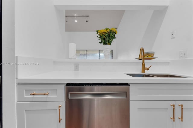 kitchen featuring white cabinets, rail lighting, light countertops, stainless steel dishwasher, and a sink