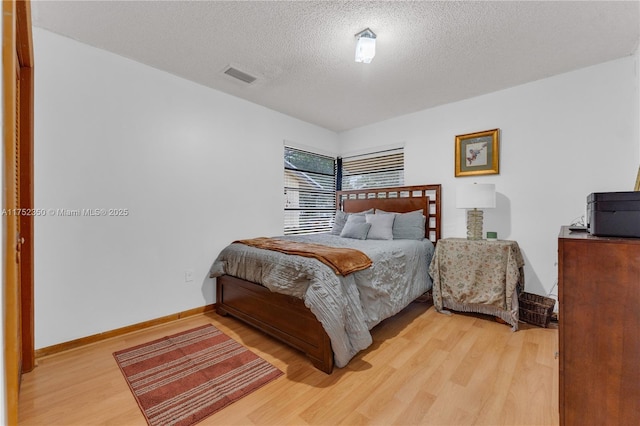 bedroom with light wood-style floors, visible vents, a textured ceiling, and baseboards