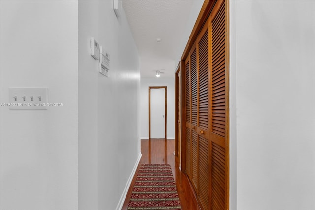 corridor featuring a textured ceiling, wood finished floors, and baseboards