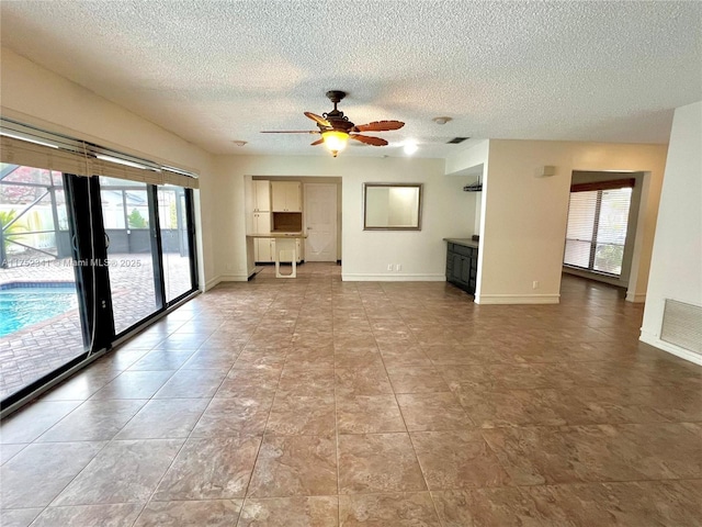 unfurnished living room with baseboards, a textured ceiling, visible vents, and a ceiling fan