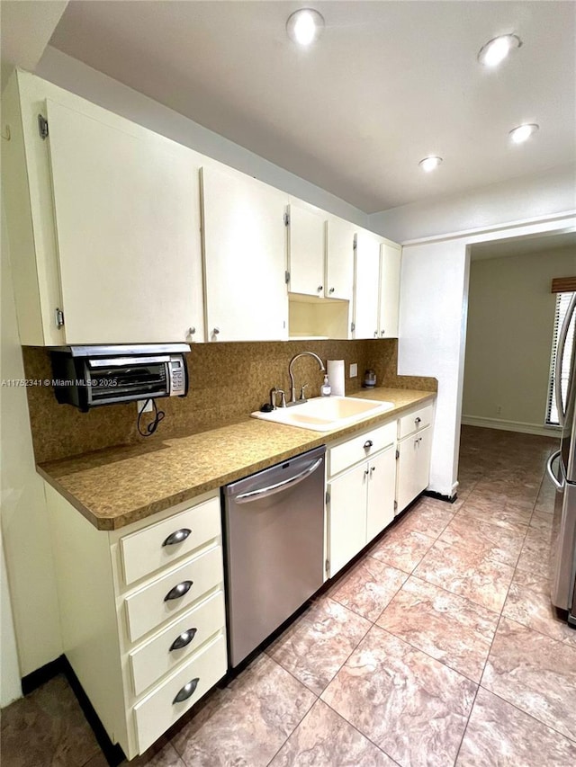 kitchen featuring appliances with stainless steel finishes, a sink, white cabinetry, and tasteful backsplash