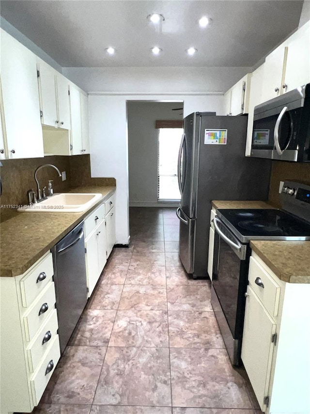 kitchen with white cabinets, appliances with stainless steel finishes, a sink, dark countertops, and backsplash