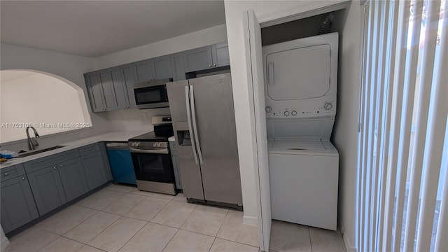 kitchen featuring stacked washer and dryer, appliances with stainless steel finishes, a sink, and light countertops