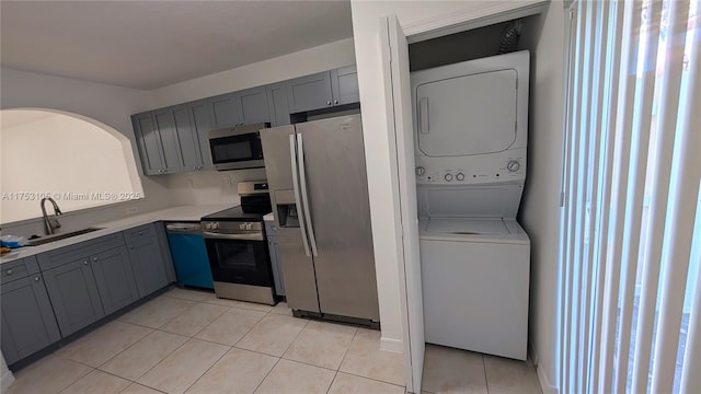 kitchen with light tile patterned floors, gray cabinetry, appliances with stainless steel finishes, stacked washer / dryer, and a sink