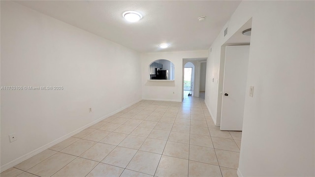 unfurnished room featuring light tile patterned floors, arched walkways, visible vents, and baseboards