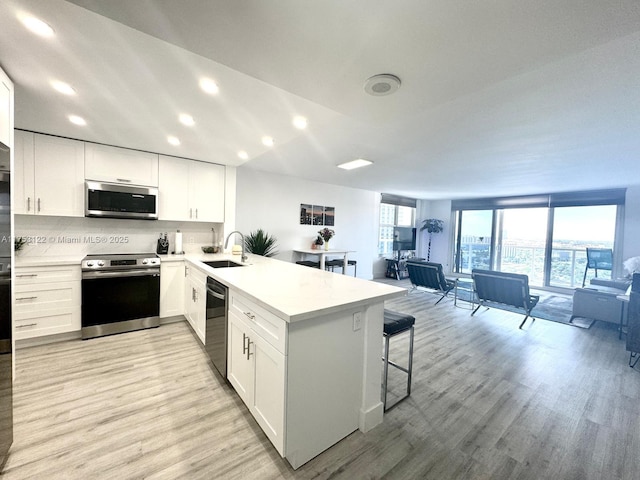 kitchen with a peninsula, stainless steel appliances, light wood-type flooring, a kitchen bar, and a sink