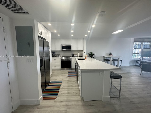 kitchen featuring visible vents, a breakfast bar, a peninsula, stainless steel appliances, and a sink