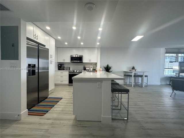 kitchen featuring a breakfast bar area, appliances with stainless steel finishes, white cabinetry, light wood-type flooring, and electric panel