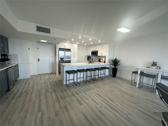 kitchen featuring stainless steel appliances, light countertops, visible vents, light wood-type flooring, and a peninsula