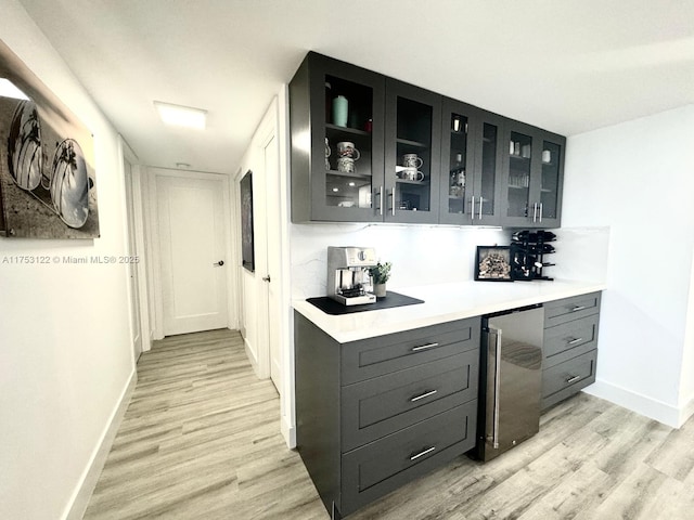 bar with baseboards, a bar, light wood finished floors, and stainless steel refrigerator