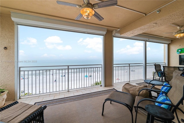 sunroom featuring a water view, a view of the beach, and a ceiling fan