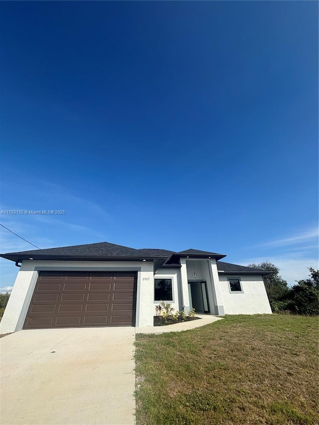 prairie-style home with concrete driveway, an attached garage, a front lawn, and stucco siding