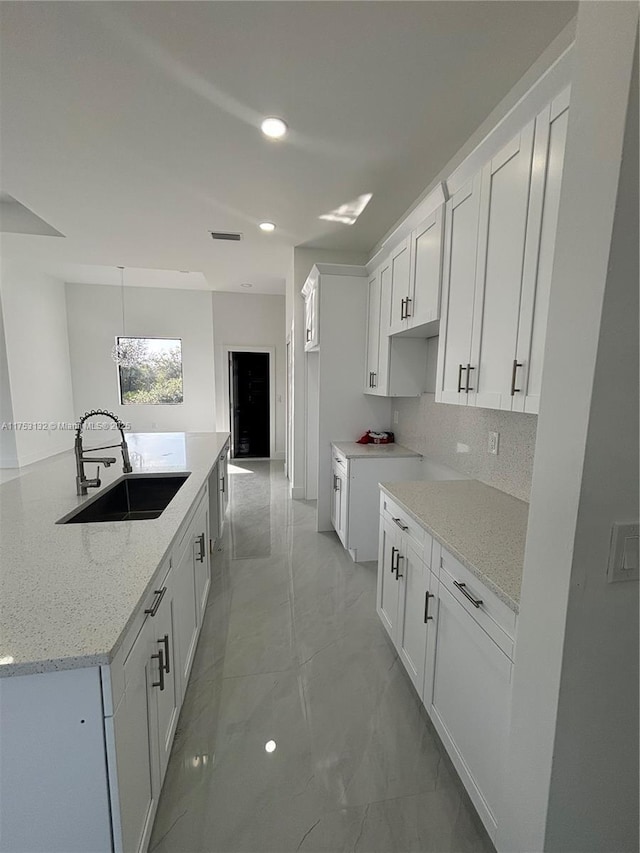 kitchen with light stone counters, white cabinetry, and a sink