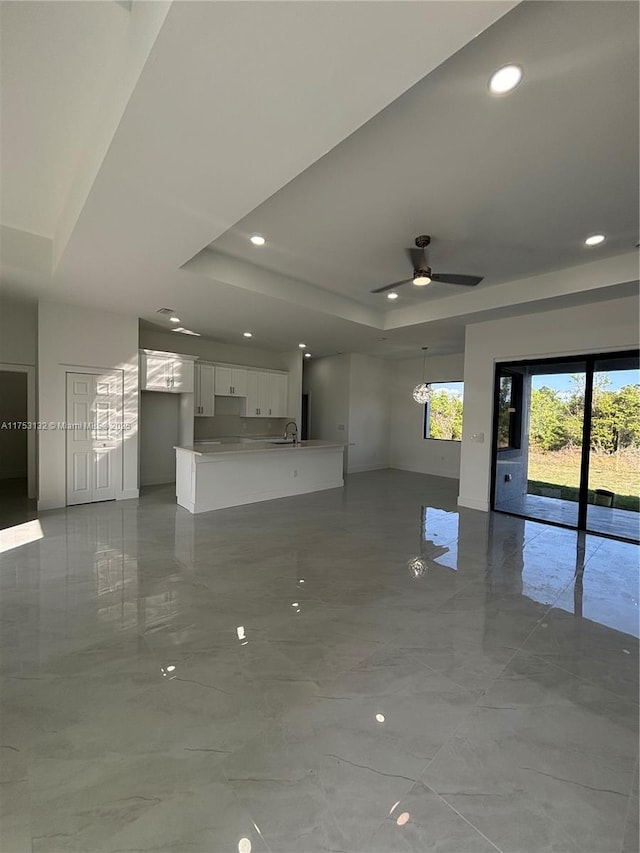 unfurnished living room with ceiling fan, marble finish floor, a tray ceiling, a sink, and recessed lighting