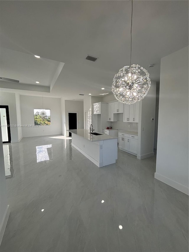 kitchen with a center island with sink, visible vents, open floor plan, white cabinets, and a sink