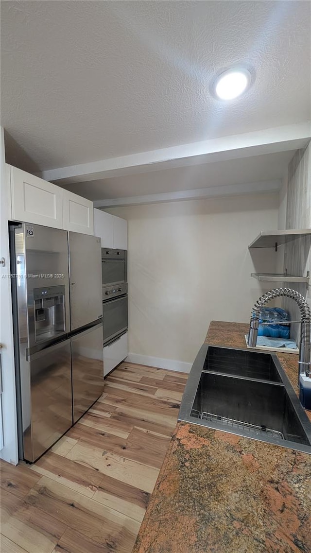 kitchen featuring white cabinetry, baseboards, light wood-type flooring, stainless steel refrigerator with ice dispenser, and beamed ceiling