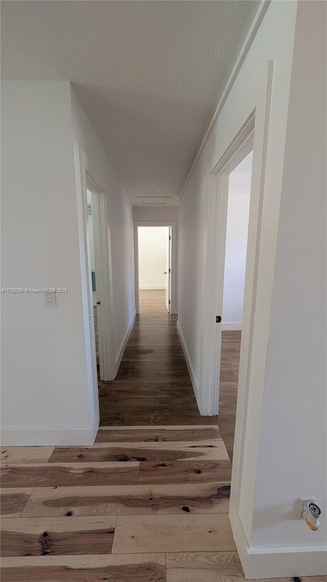 corridor featuring wood-type flooring, a textured ceiling, and baseboards
