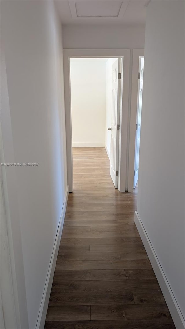 corridor featuring baseboards, attic access, and dark wood-type flooring