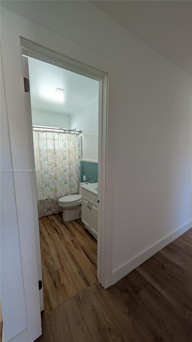 bathroom featuring toilet, curtained shower, wood finished floors, and vanity
