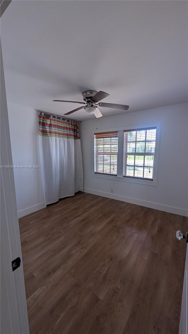 spare room with a ceiling fan, baseboards, and dark wood finished floors
