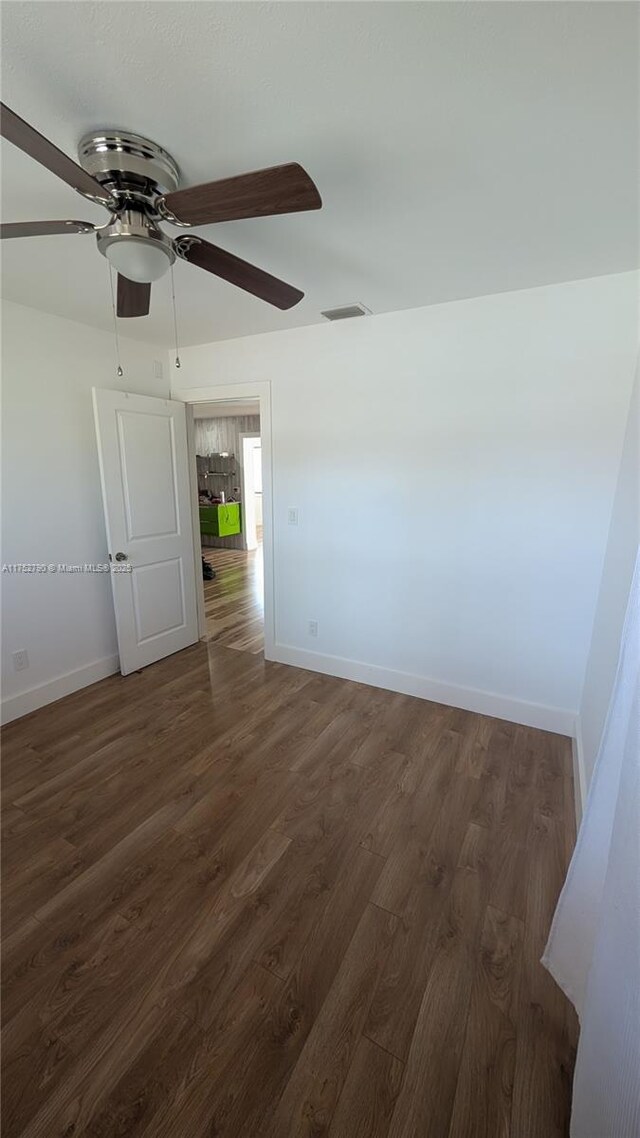 spare room featuring visible vents, baseboards, dark wood-style flooring, and ceiling fan