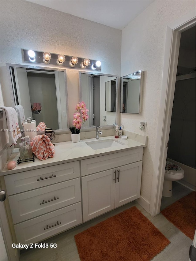 bathroom with toilet, a textured wall, and vanity