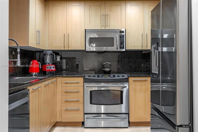 kitchen featuring appliances with stainless steel finishes, a sink, dark stone countertops, and tasteful backsplash