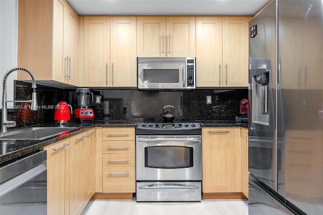 kitchen with tasteful backsplash, dark stone counters, appliances with stainless steel finishes, light brown cabinetry, and a sink