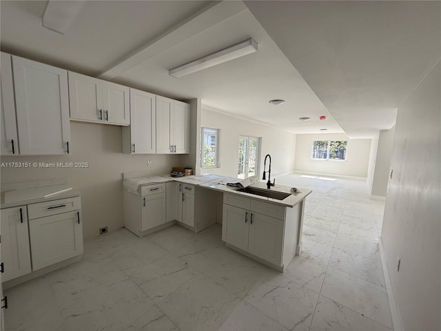 kitchen featuring marble finish floor, open floor plan, white cabinetry, a sink, and a peninsula