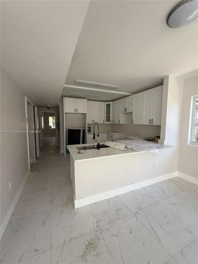 kitchen featuring marble finish floor, white cabinetry, a sink, and baseboards