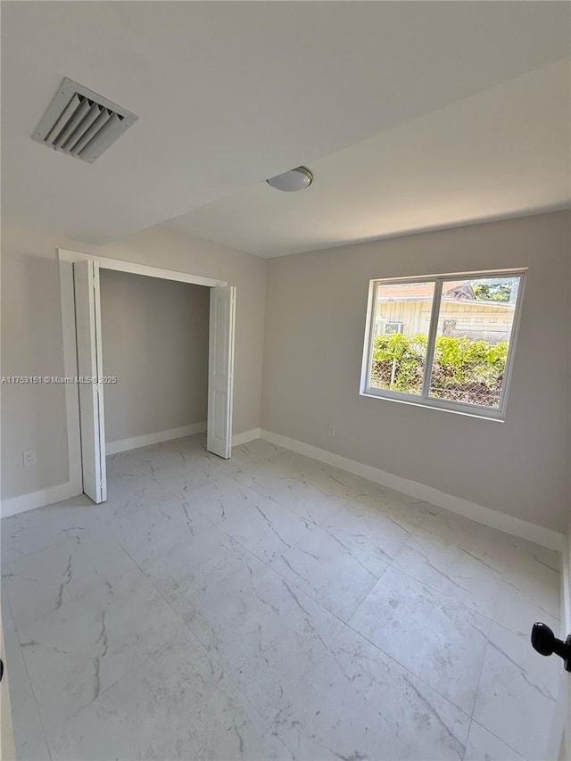 unfurnished bedroom with a closet, marble finish floor, visible vents, and baseboards