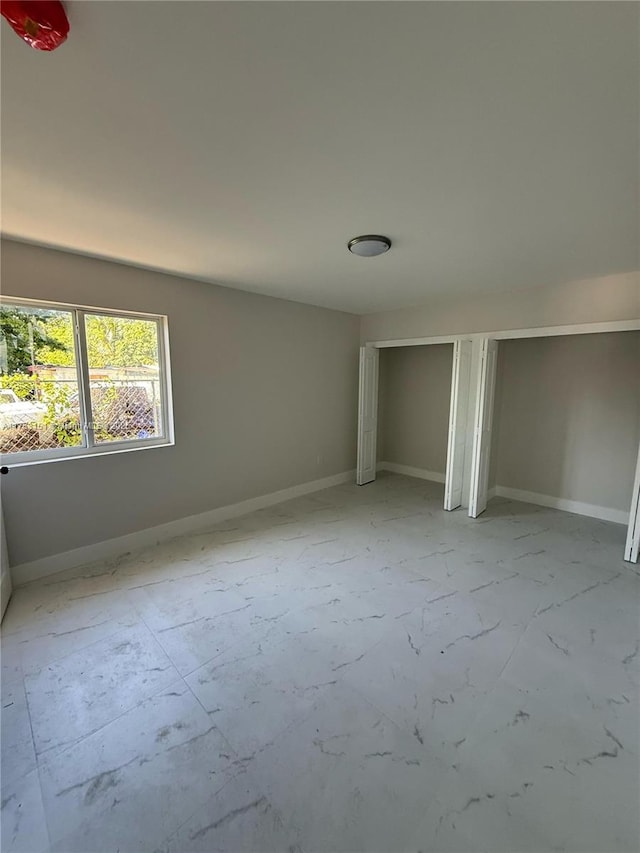 unfurnished bedroom with marble finish floor, baseboards, and two closets