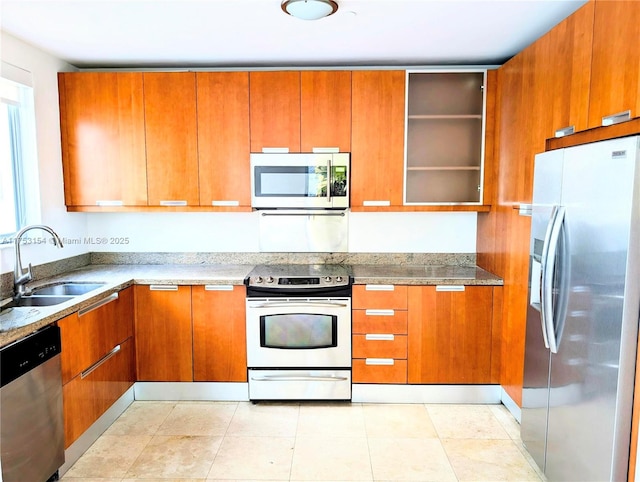 kitchen featuring light tile patterned floors, appliances with stainless steel finishes, brown cabinets, light stone countertops, and a sink