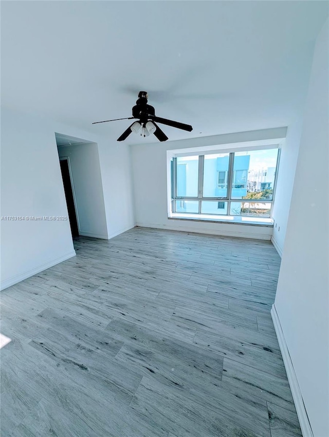 spare room featuring wood finished floors, a ceiling fan, and baseboards