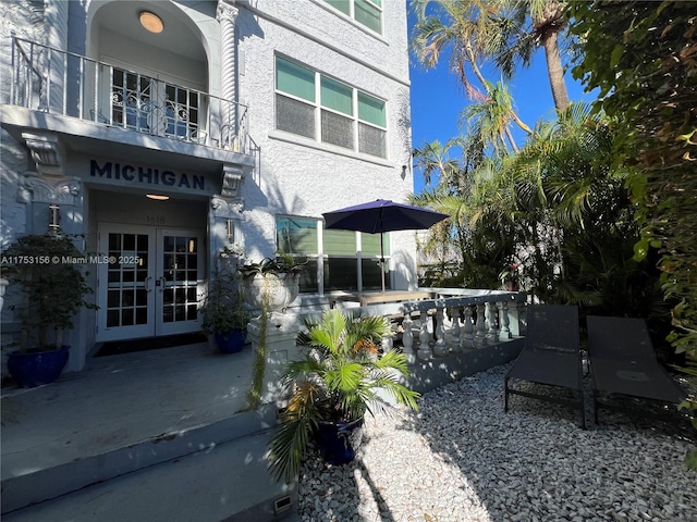 exterior space with a balcony, stucco siding, and french doors