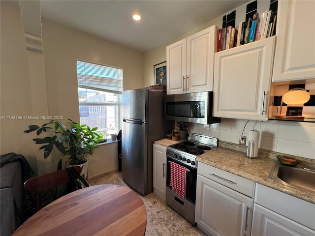 kitchen with appliances with stainless steel finishes, white cabinets, a sink, and decorative backsplash