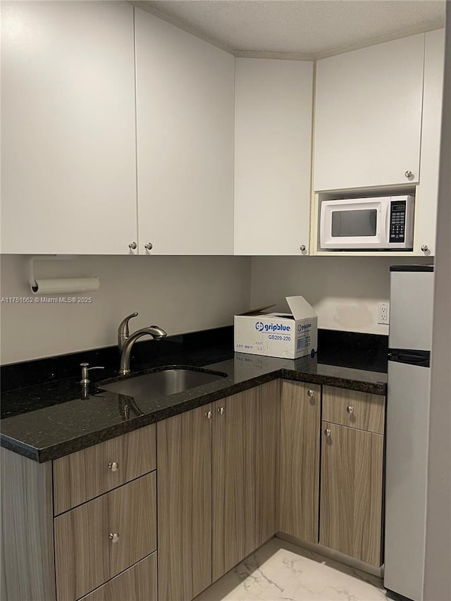 kitchen with white microwave, dark stone countertops, freestanding refrigerator, marble finish floor, and a sink