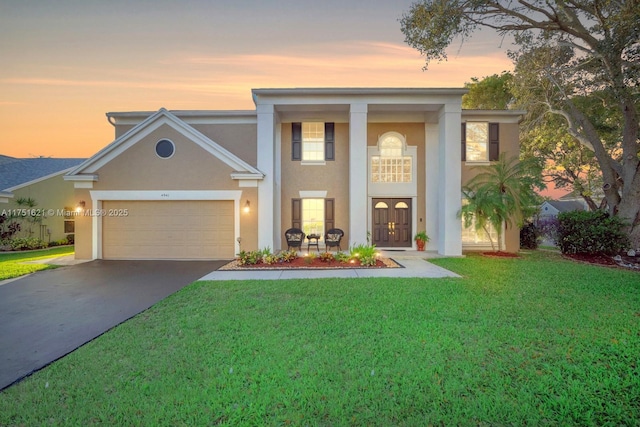 greek revival inspired property with an attached garage, driveway, a yard, french doors, and stucco siding