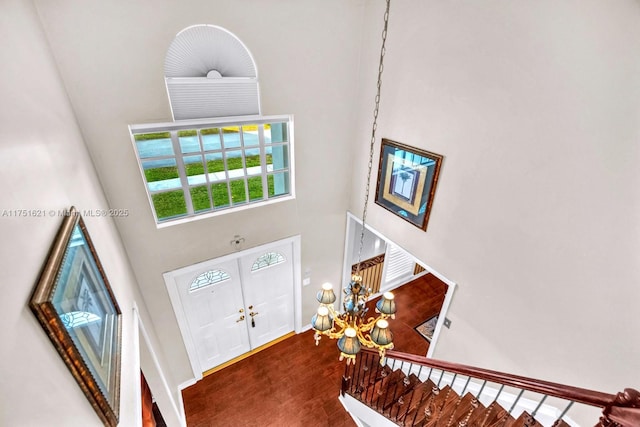 foyer entrance with baseboards, wood finished floors, a towering ceiling, and a notable chandelier