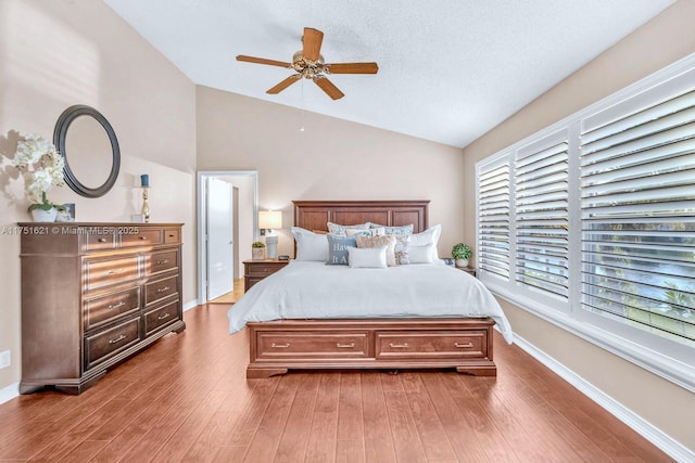 bedroom featuring lofted ceiling, a textured ceiling, wood finished floors, a ceiling fan, and baseboards